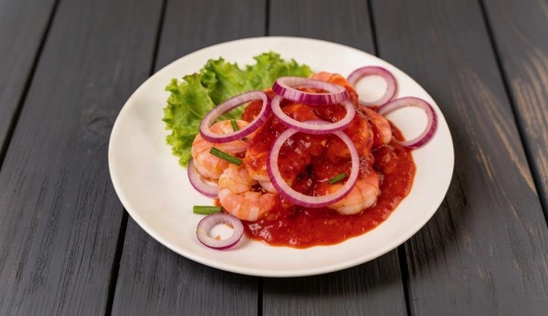 Ceviche Camarones en salsa de tomate, cebolla roja, cilantro, patacones o galleta.